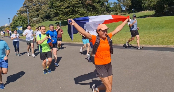 Woman wearing orange shirt surrounded by people running on road. She's holding a French Flag 