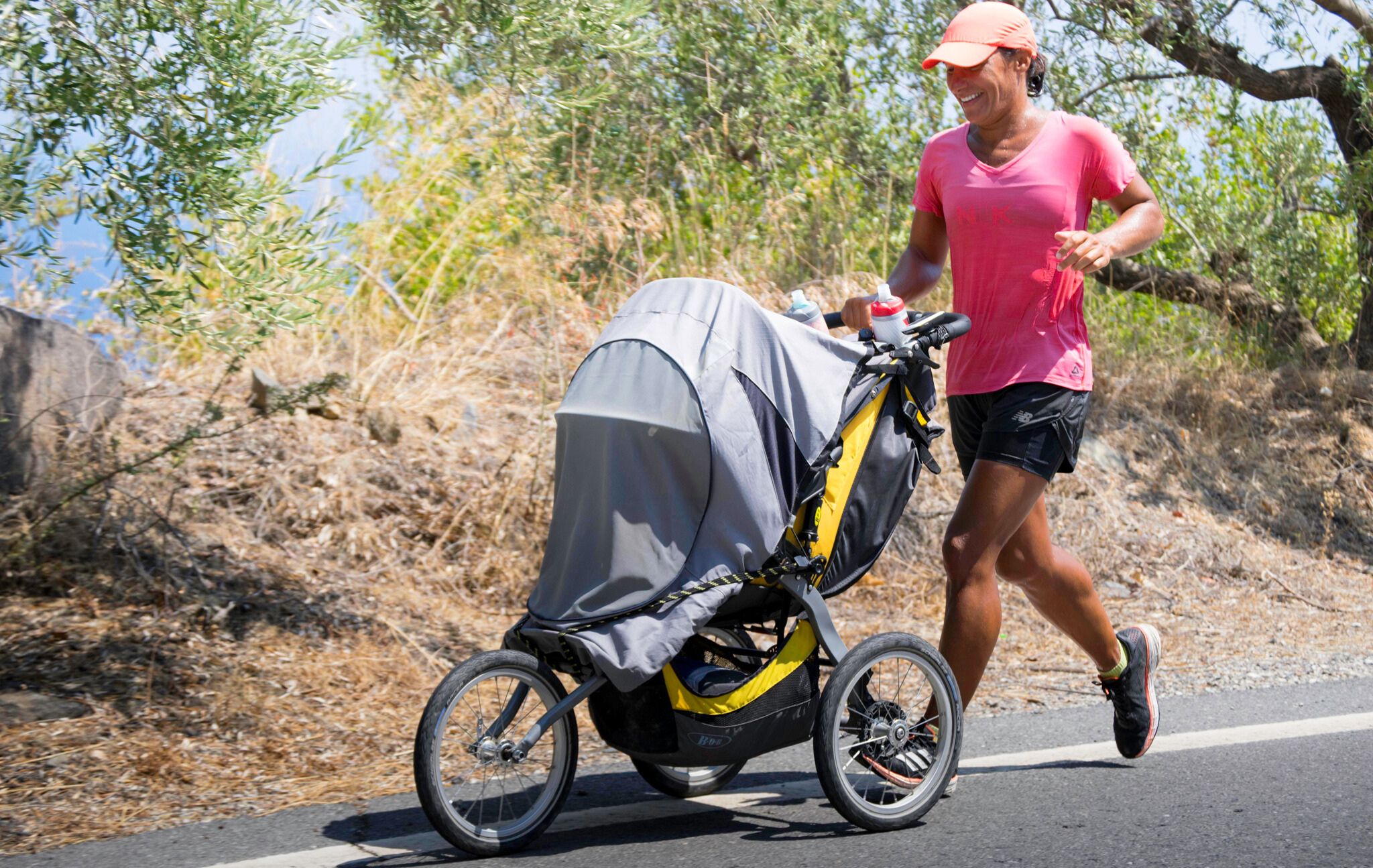 Woman in pink shirt runs on road pushing a baby stroller