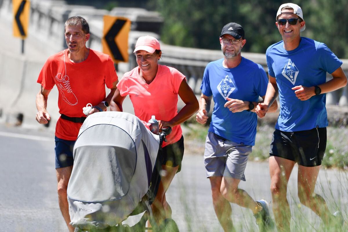 Four people run down a street together, with a woman pushing a stroller. 