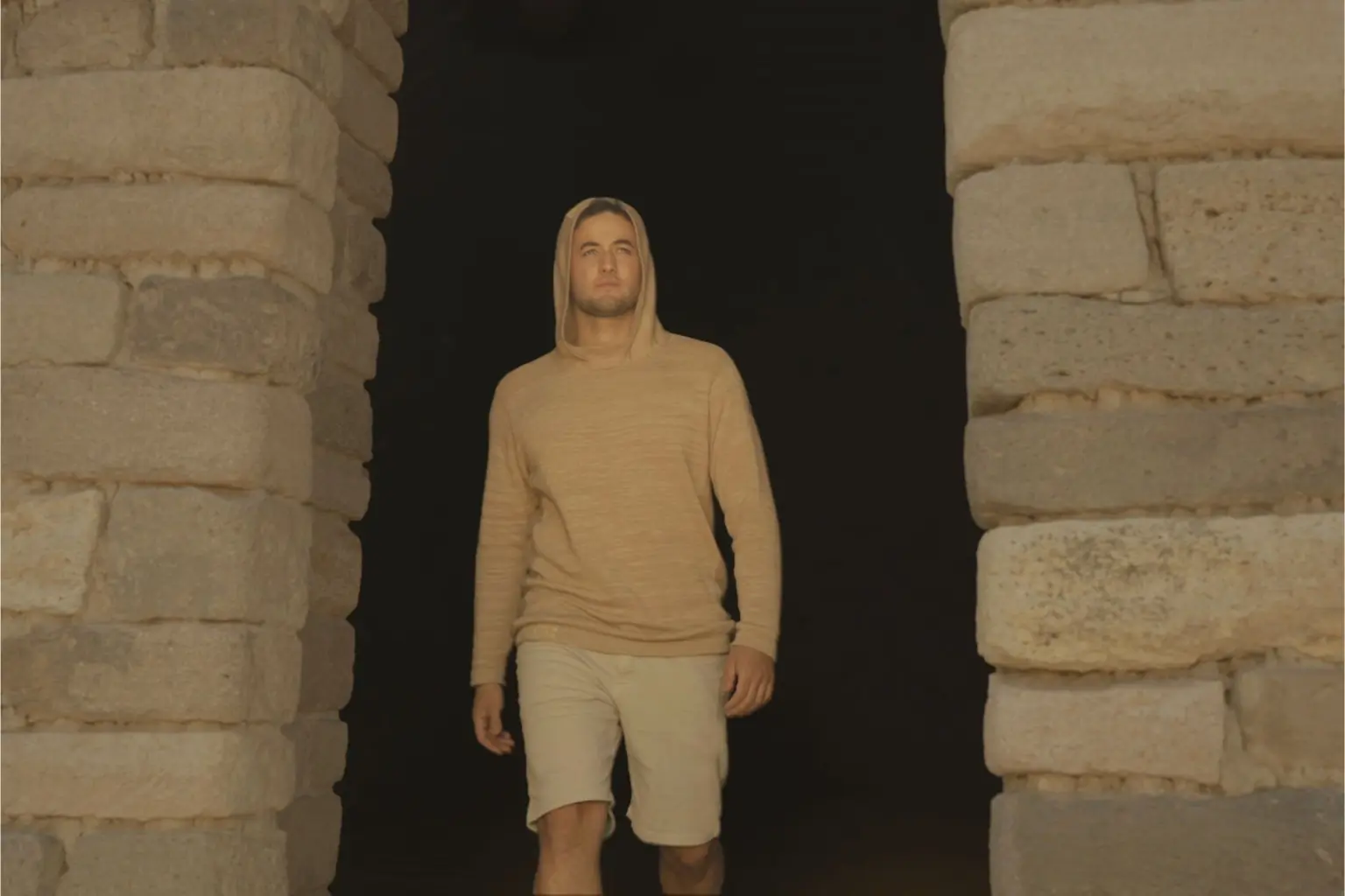 Person walks out of brick doorframe wearing light brown knit hoodie