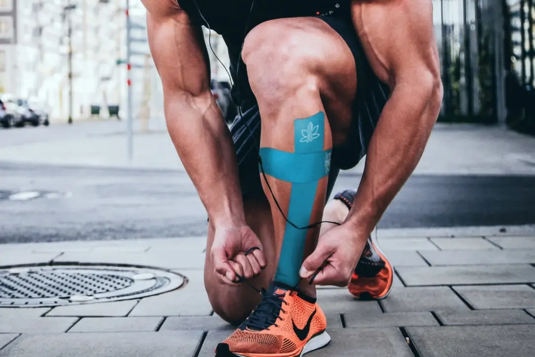 Close up of person ready for a run tying their shoes with blue KT tape on.  