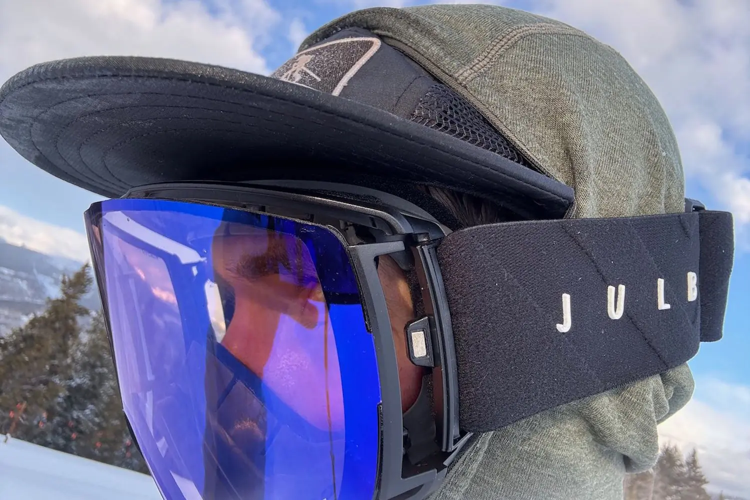 Close-up of a person wearing Julbo Cyrius ski goggles with a mirrored blue lens and black strap, showing side ventilation