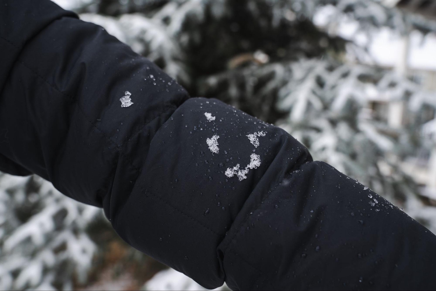 Close-up of a black REI Co-op Norseland Down Parka sleeve with snowflakes and water droplets on the fabric