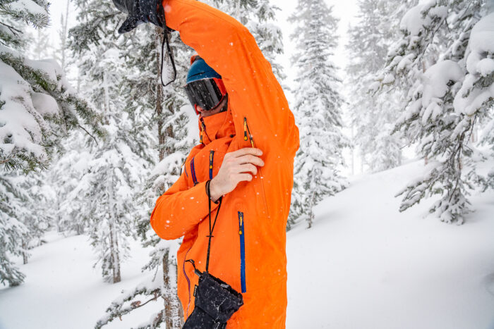 man pulling down zipper on armpit vent in snowboard jacket