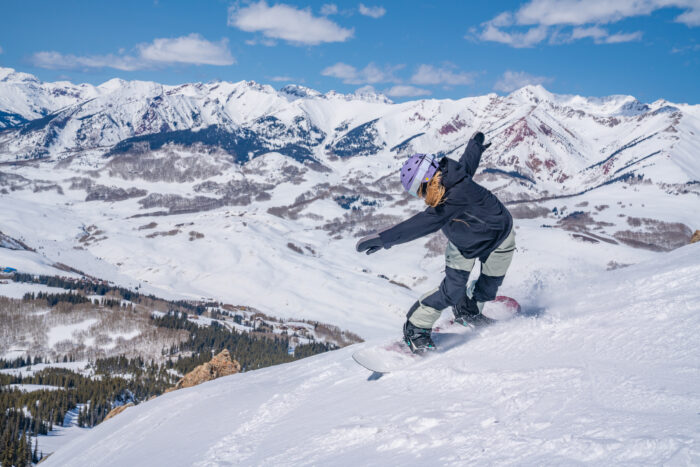 snowboarder takes front edge slash with mountains as a backdrop