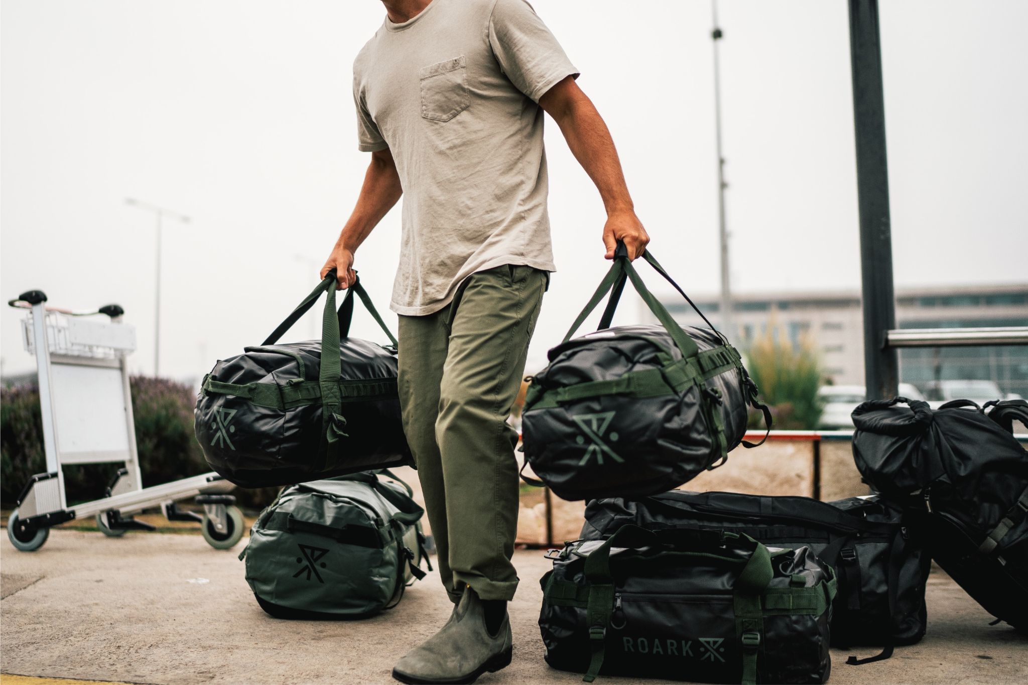 Person wearing white t-shirt and green pants loads duffel bags
