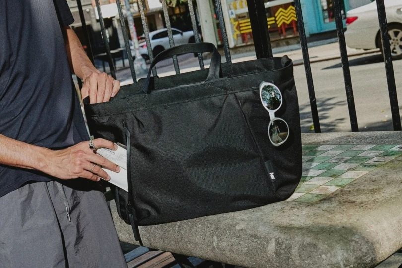 Close up shot of person putting wallet into pocket of large black tote bag.