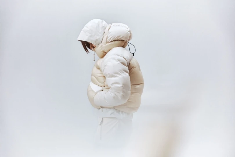 Person wears big white puffy jacket on white background.