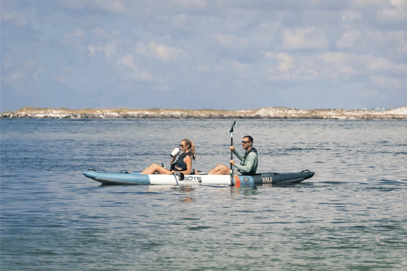 Two people sit in a kayak and paddle on the water
