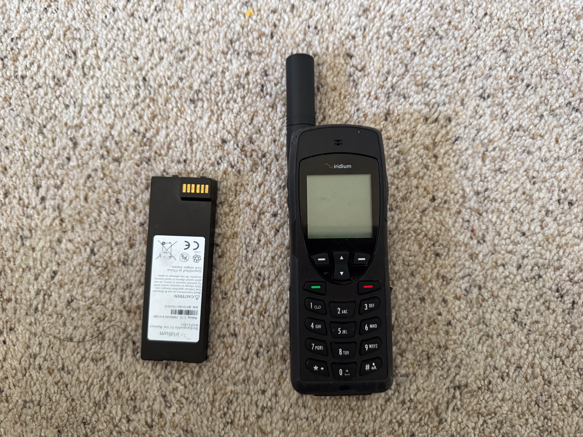 the iridium 9555 satellite phone beside an extra battery on a carpeted floor