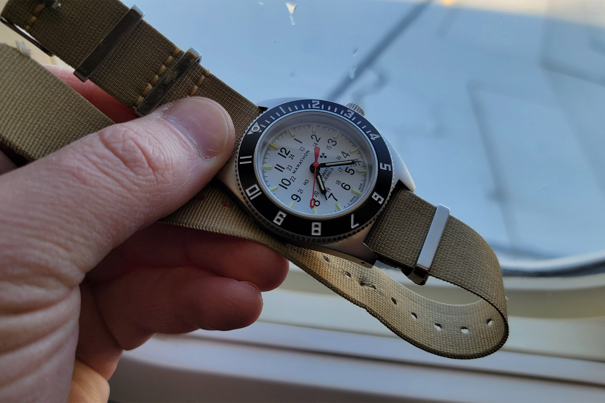 The Marathon SSNAV-D Auto Arctic Edition held near an airplane window on a tan strap during flight