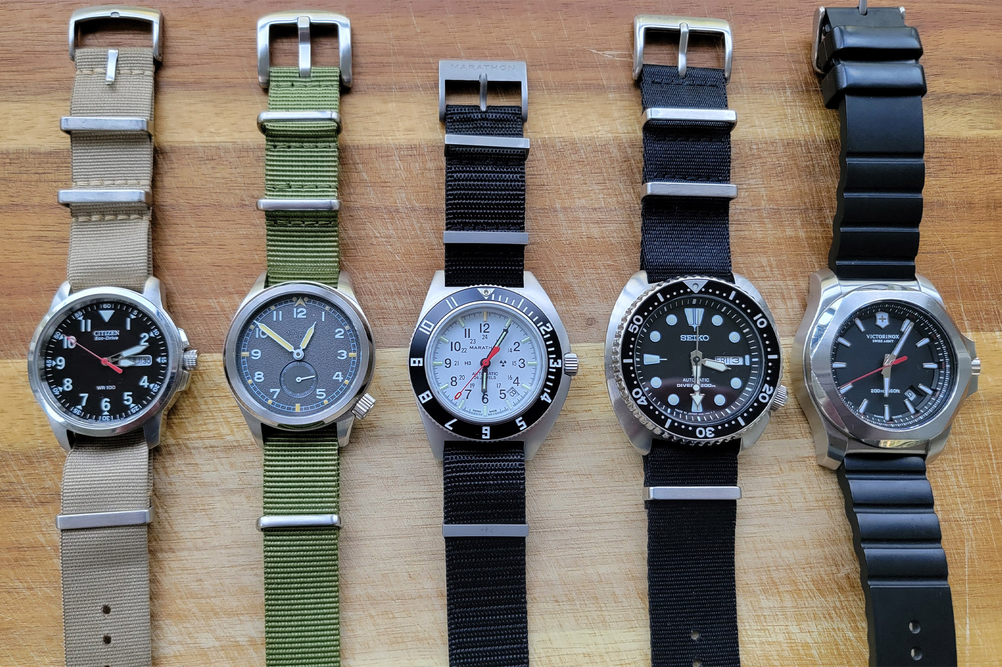 The Marathon SSNAV-D Auto Arctic Edition shown centered among four other pilot and field watches on a wooden surface