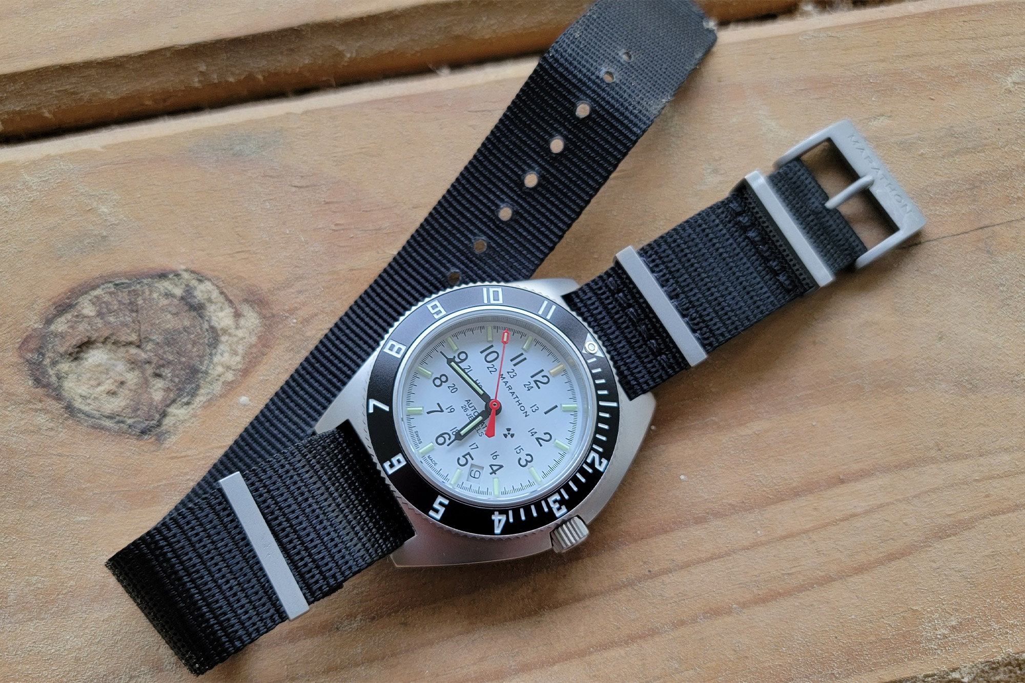 The Marathon SSNAV-D Auto Arctic Edition laid flat on a wooden surface with its black strap unbuckled