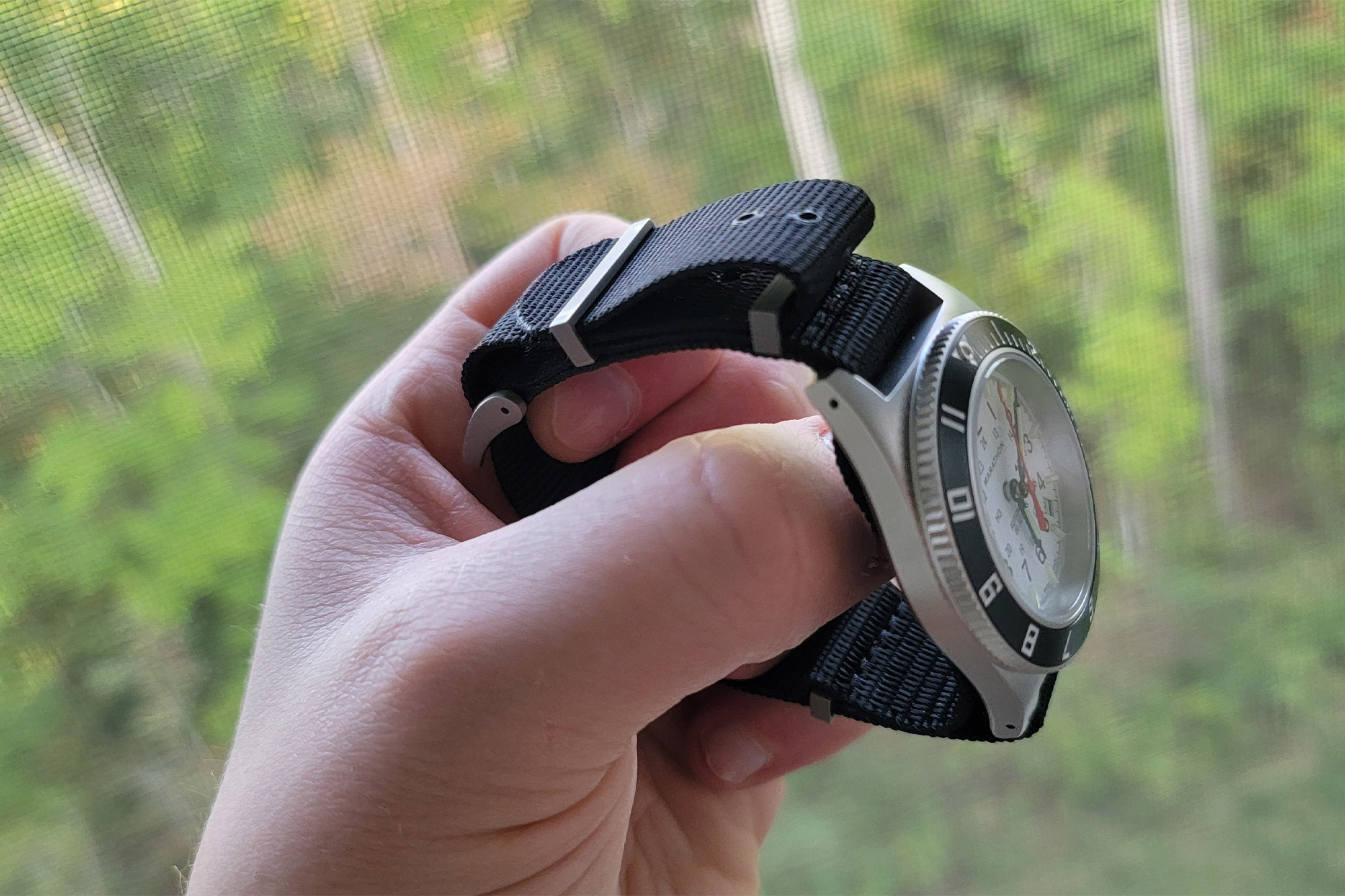 A close side view of the Marathon SSNAV-D Auto Arctic Edition held in hand, showing the curved case and nylon strap