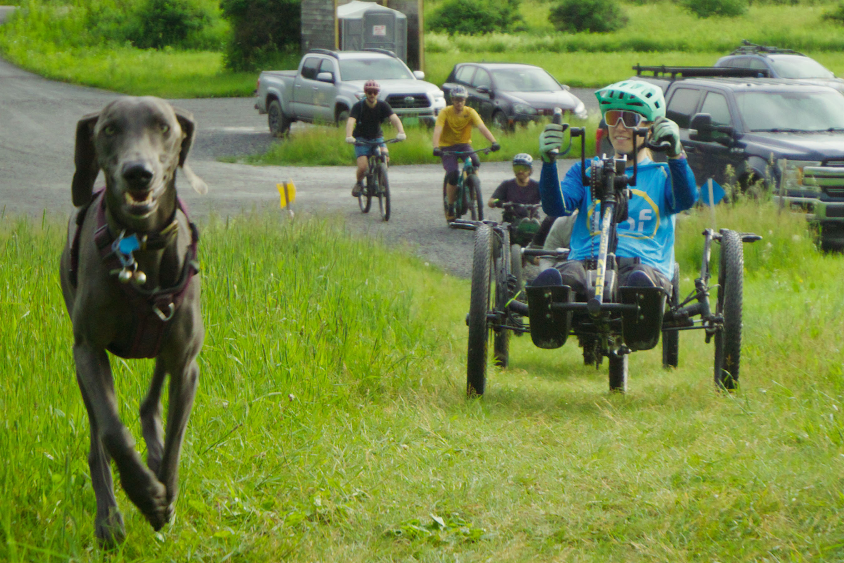 Dog, adaptive rider, and other riders ride on grass trail