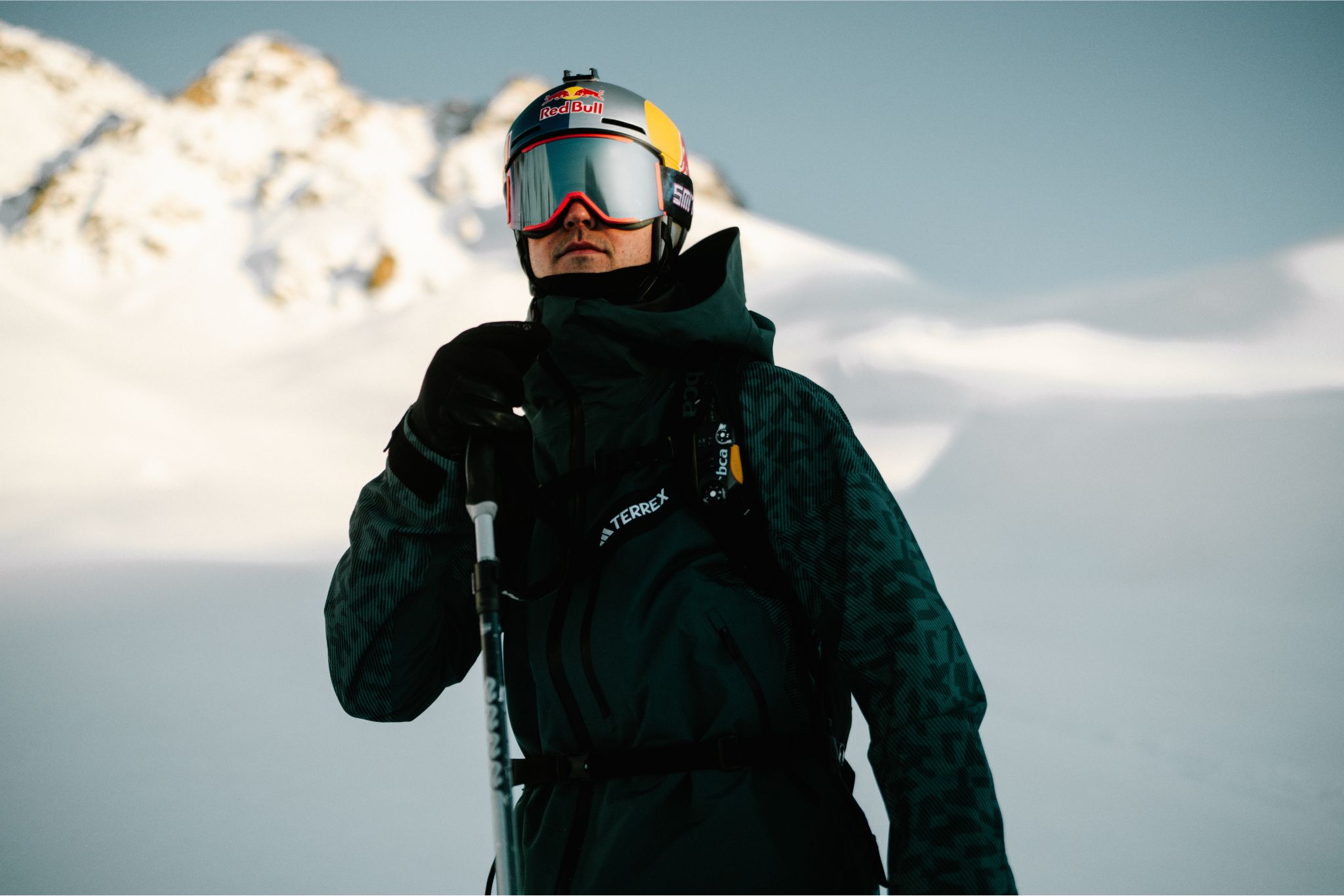 Skier stands wearing jacket and goggles on snowy mountain. 