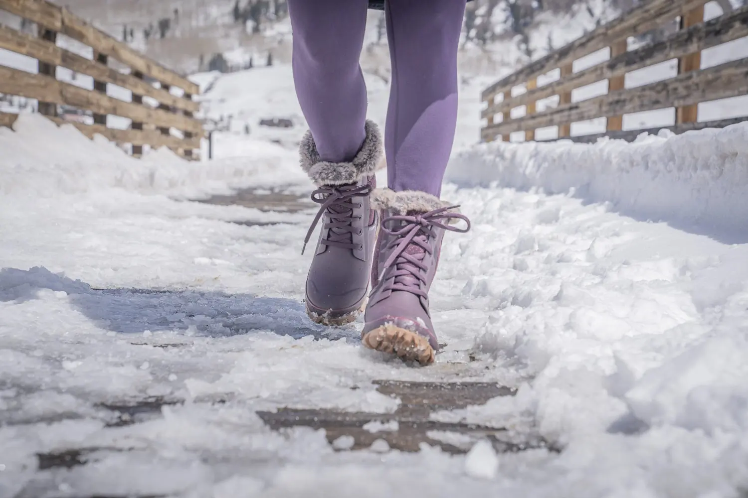 Person wearing purple Bogs Arcata Faded boots walking on a snow-covered wooden path