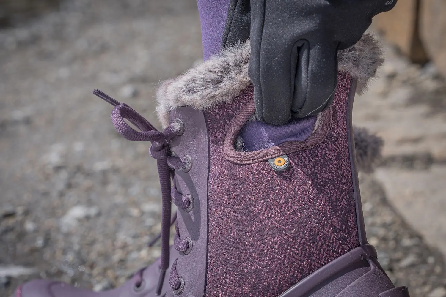 Close-up of a person pulling on a Bogs Arcata Faded waterproof winter boot with faux fur lining