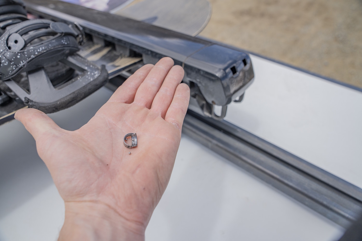 Close-up of a hand holding a small broken metal component from a Kuat Grip 6 Ski/Snowboard Rack