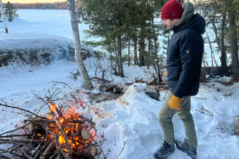 man standing next to campfire by frozen lake