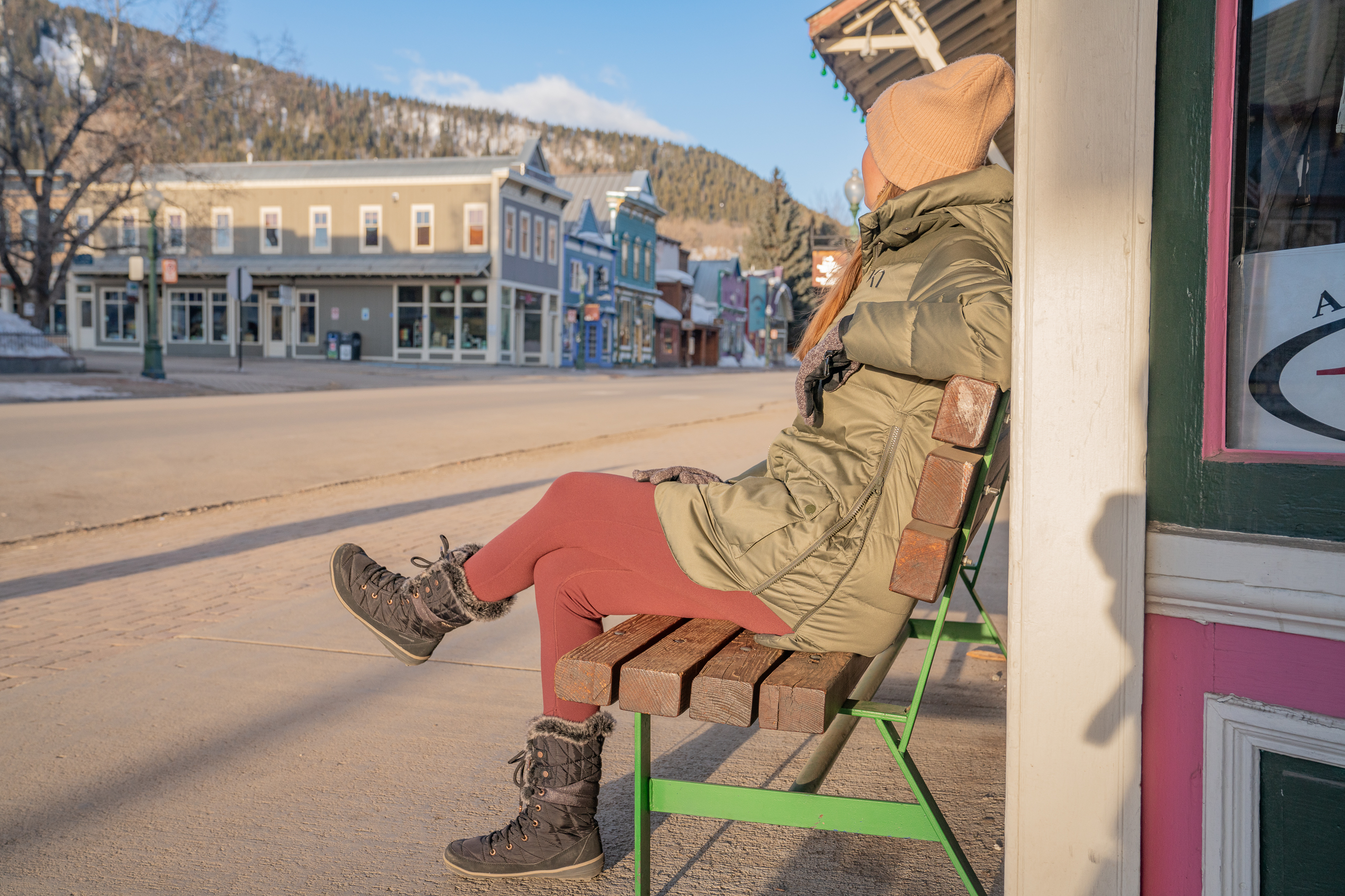 Woman wearing winter parka sitting on storefront bench