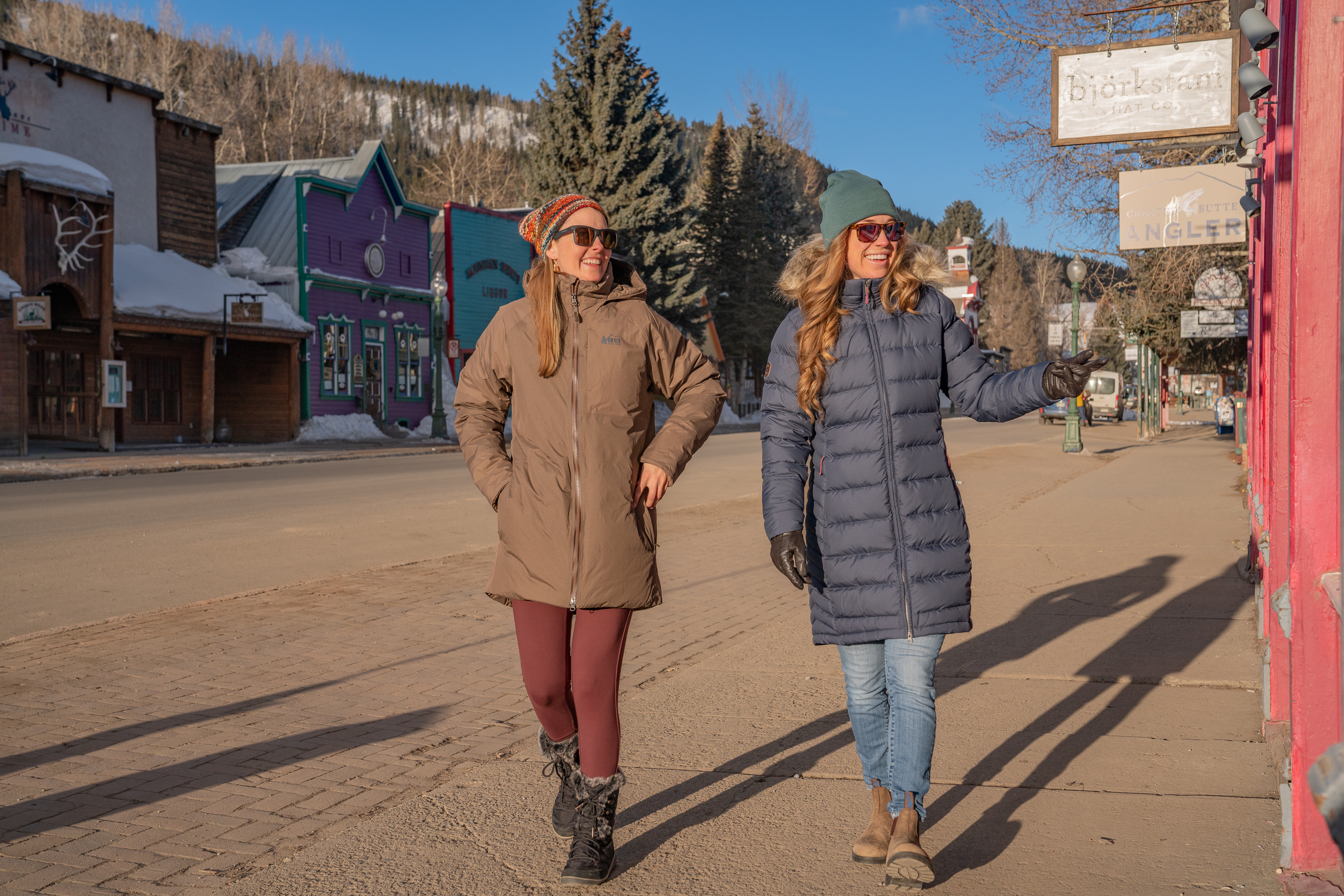 Two women walking in winter coats down the main street in a mountain town 