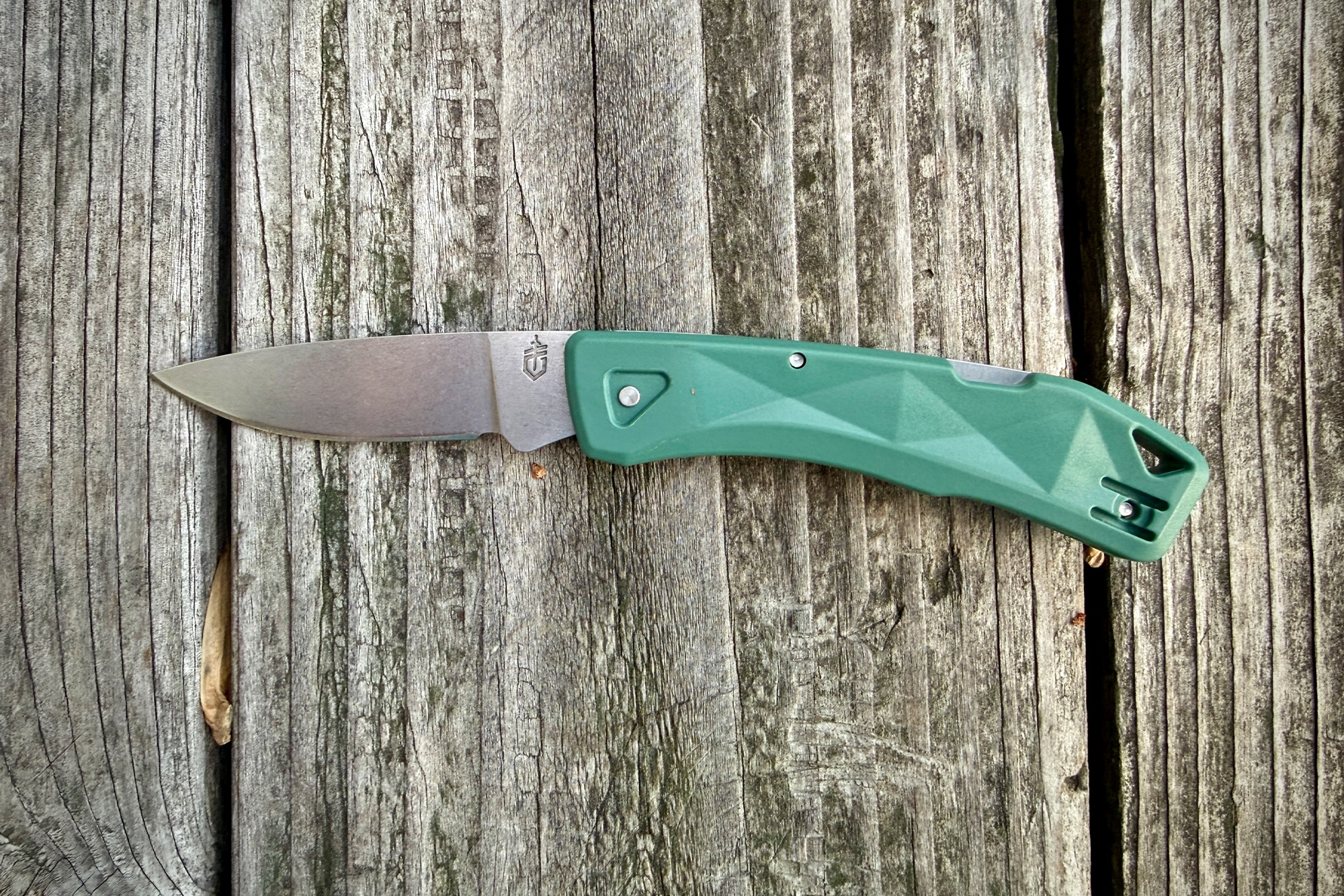 The Gerber LST Ultra shown fully opened on weathered wooden boards, highlighting its simple blade and green handle