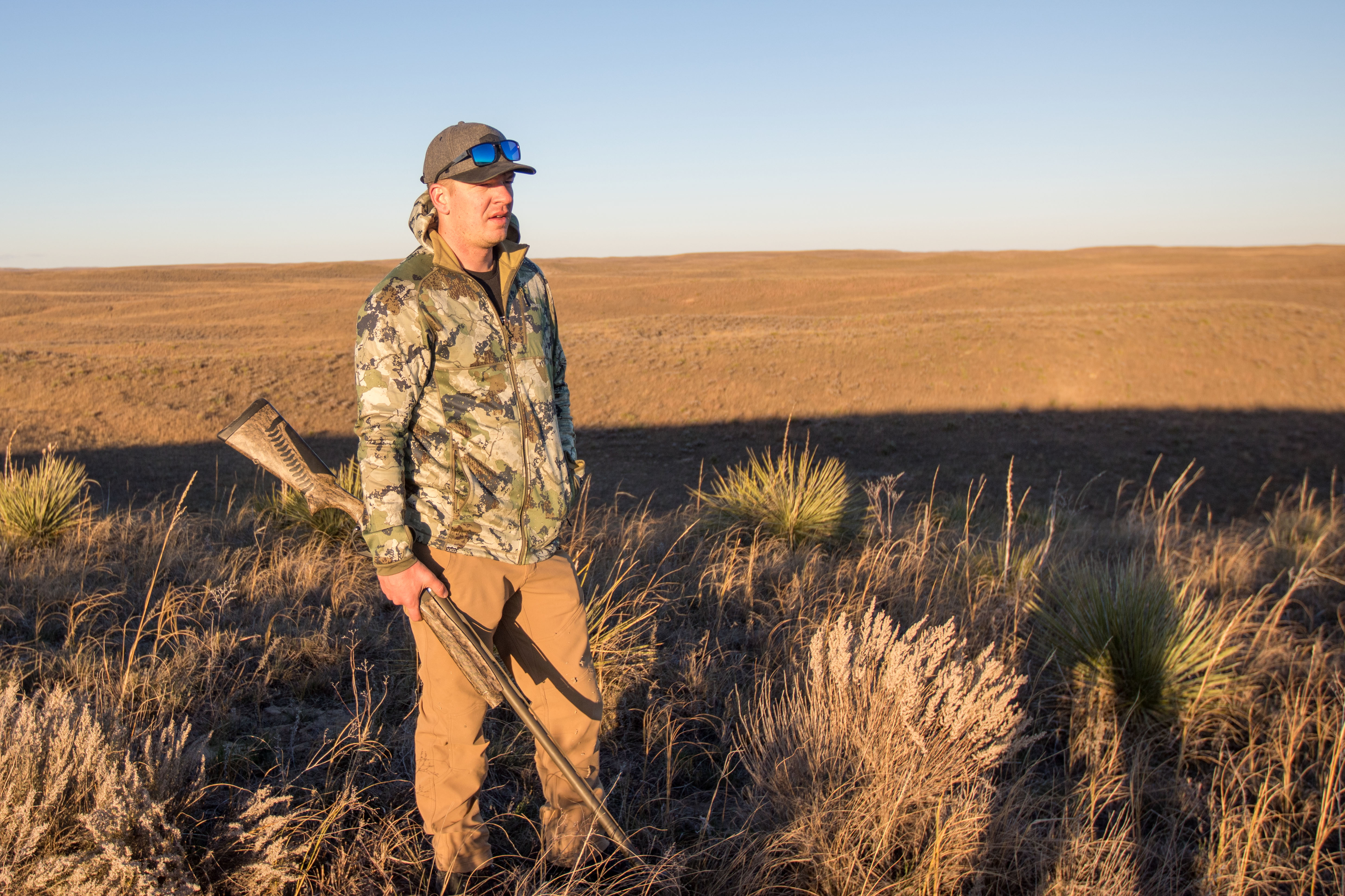 A hunter on top of a hill in the plains holding a shotgun.