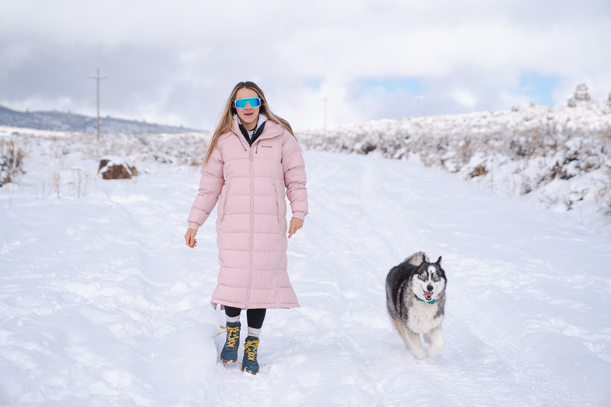 woman walking in calf-length winter jacket with Husky dog
