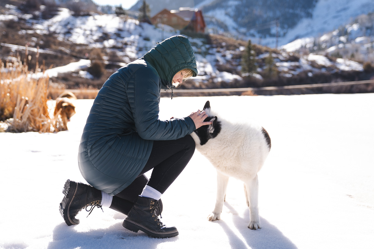 woman petting dog while testing winter jacket 