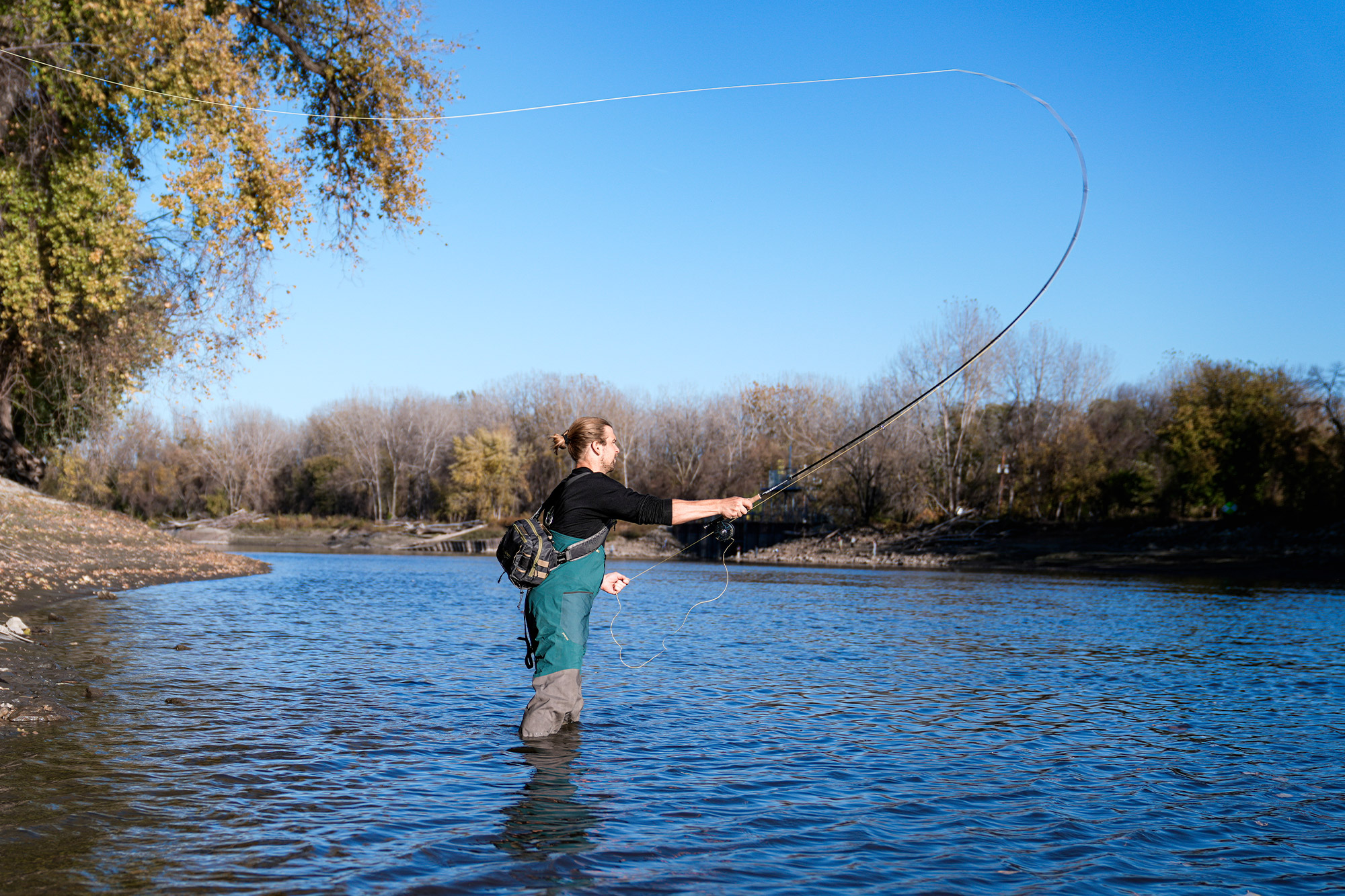 Angler fly casting in the middle of a clear river on a sunny day