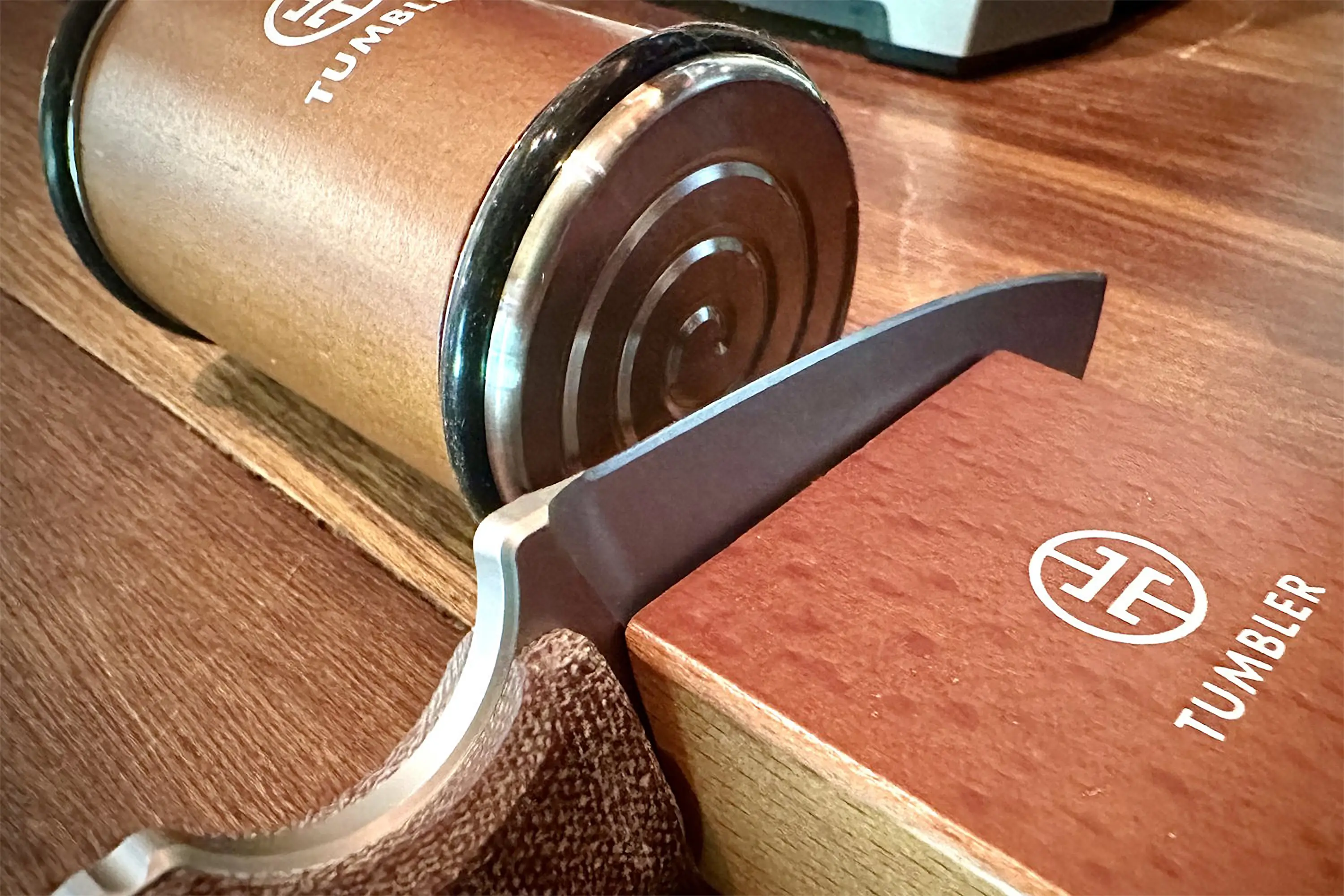 Stainless steel helix-shaped tumbler lying on its side on a wooden surface next to a Tumbler knife sharpener