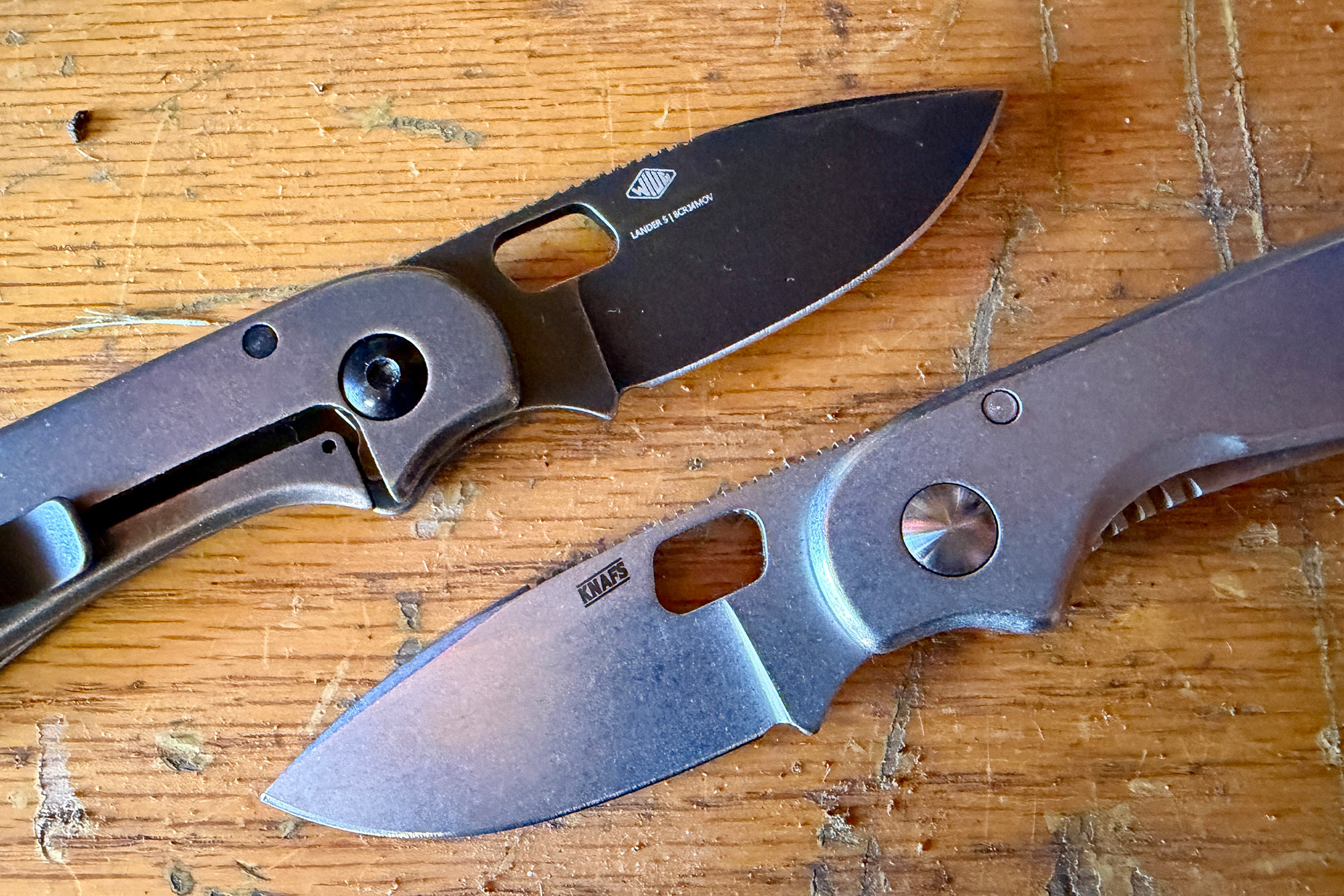 Both versions of the Lander knife shown on a workbench with their blades open
