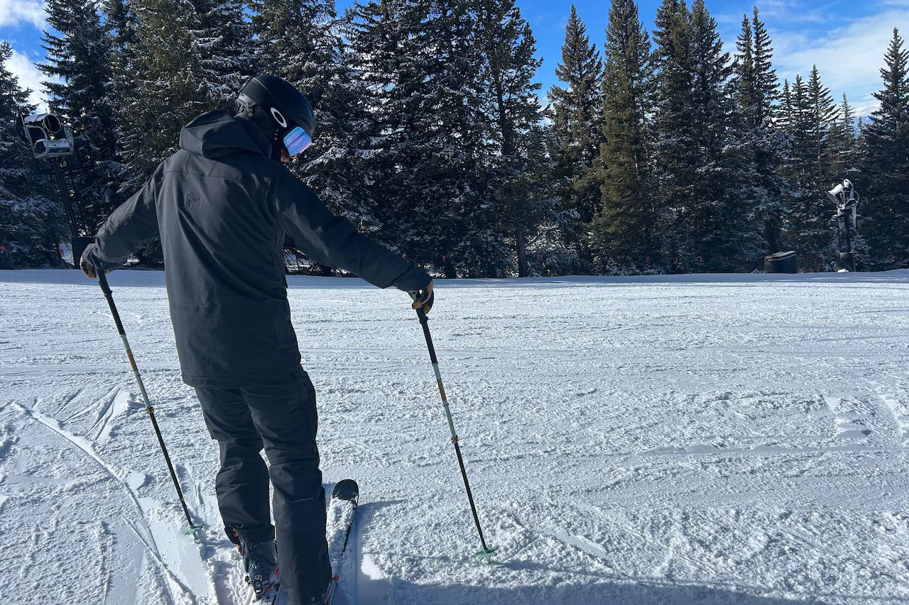 Rear view of the Norrona ski jacket and pants while standing on groomed snow