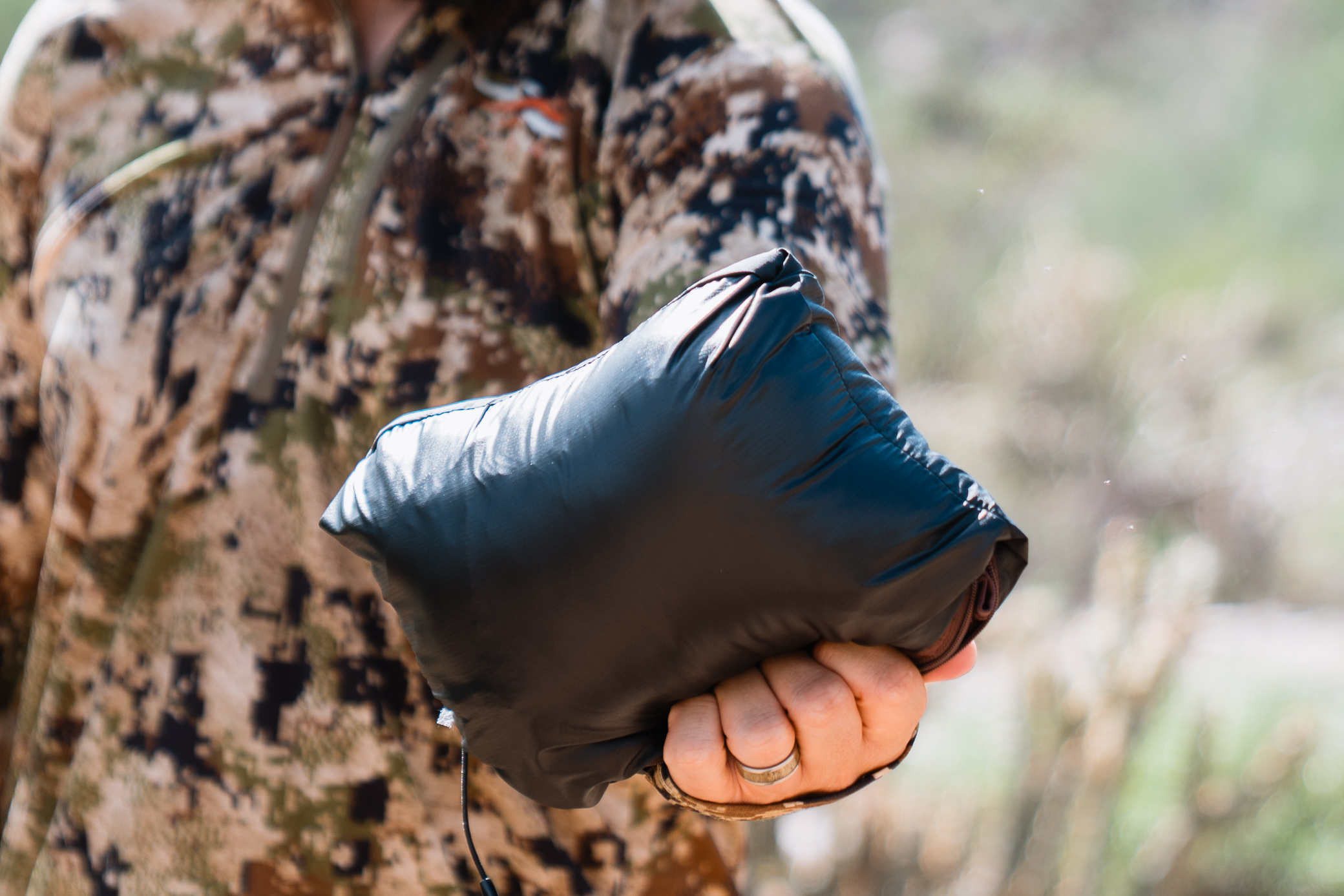 A hand holds the Sitka MicroDown Hooded Jacket packed tightly into a small bundle