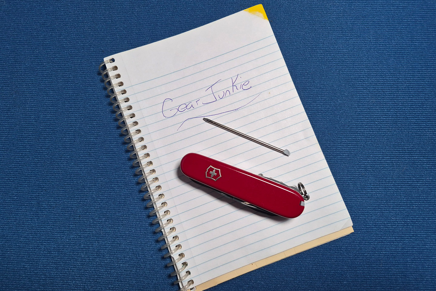 A red Victorinox and its metal pin lay on a notebook that has “Gear Junkie” written on the page