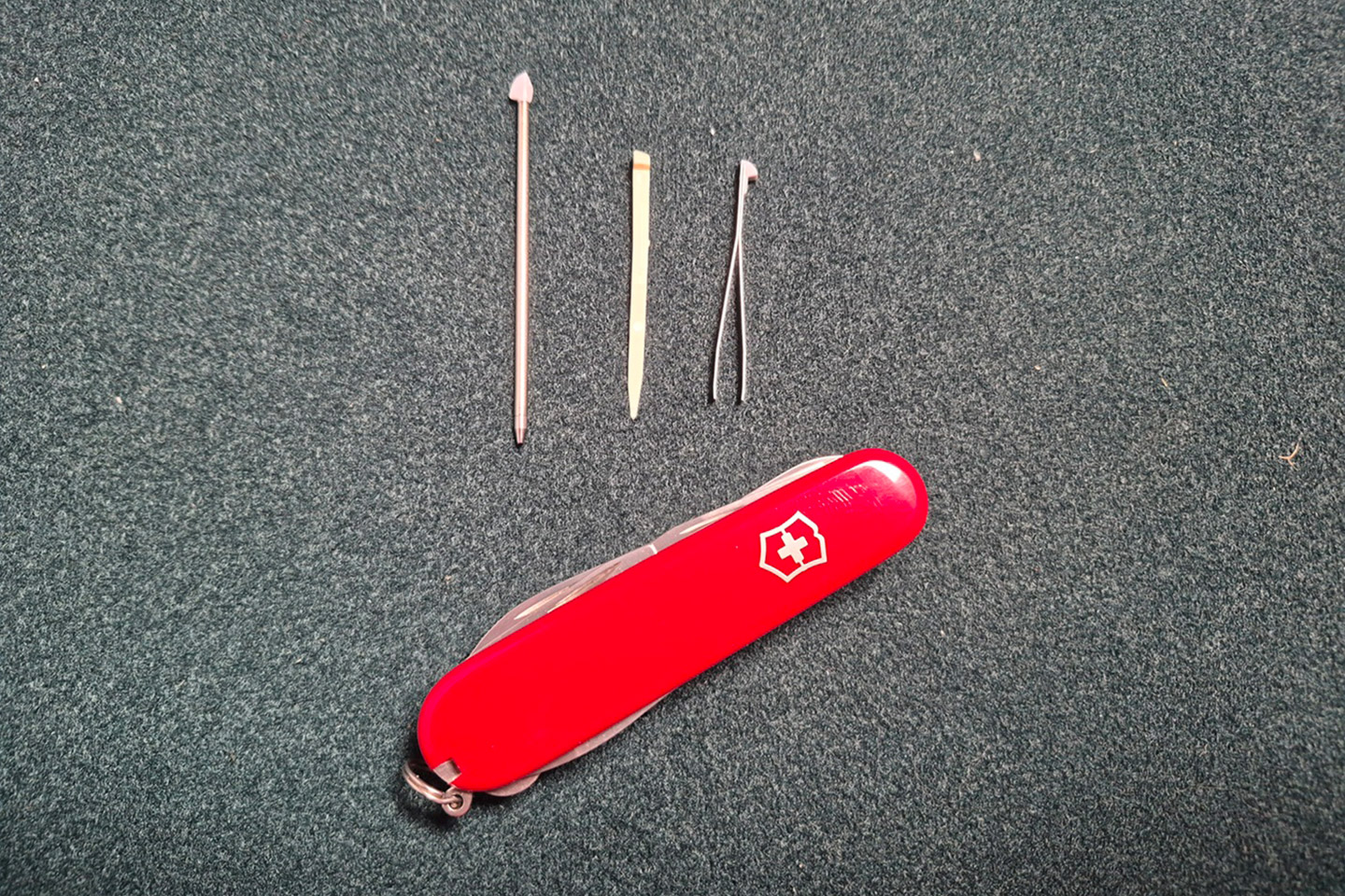 The Victorinox Swiss Army Companion rests beside its small tools—pin, toothpick, and tweezers—laid out on a dark fabric