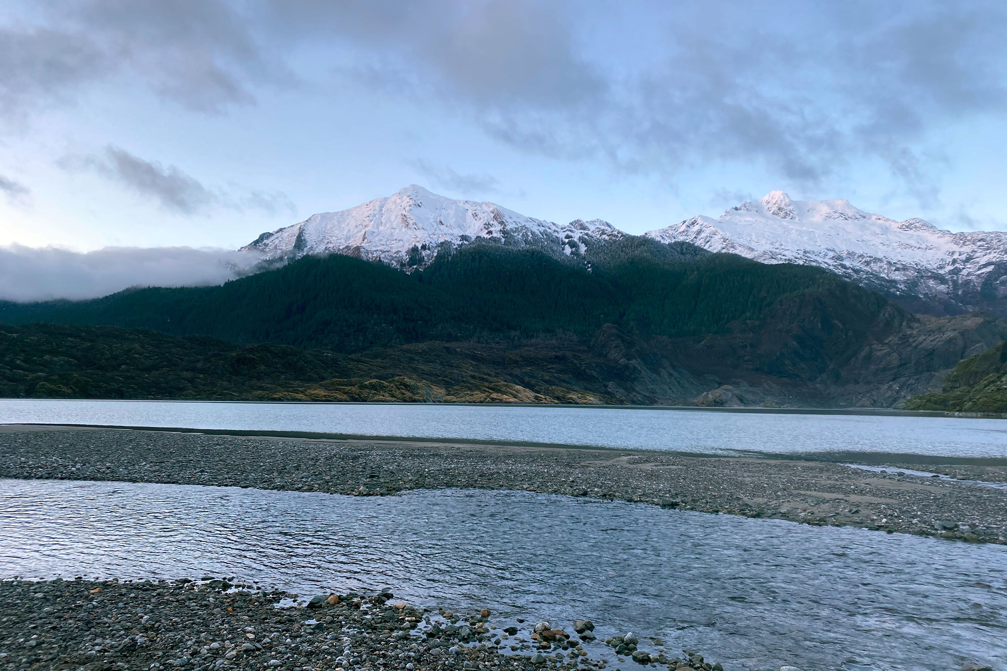 A wide river flows below snow-covered mountains near Juneau, Alaska