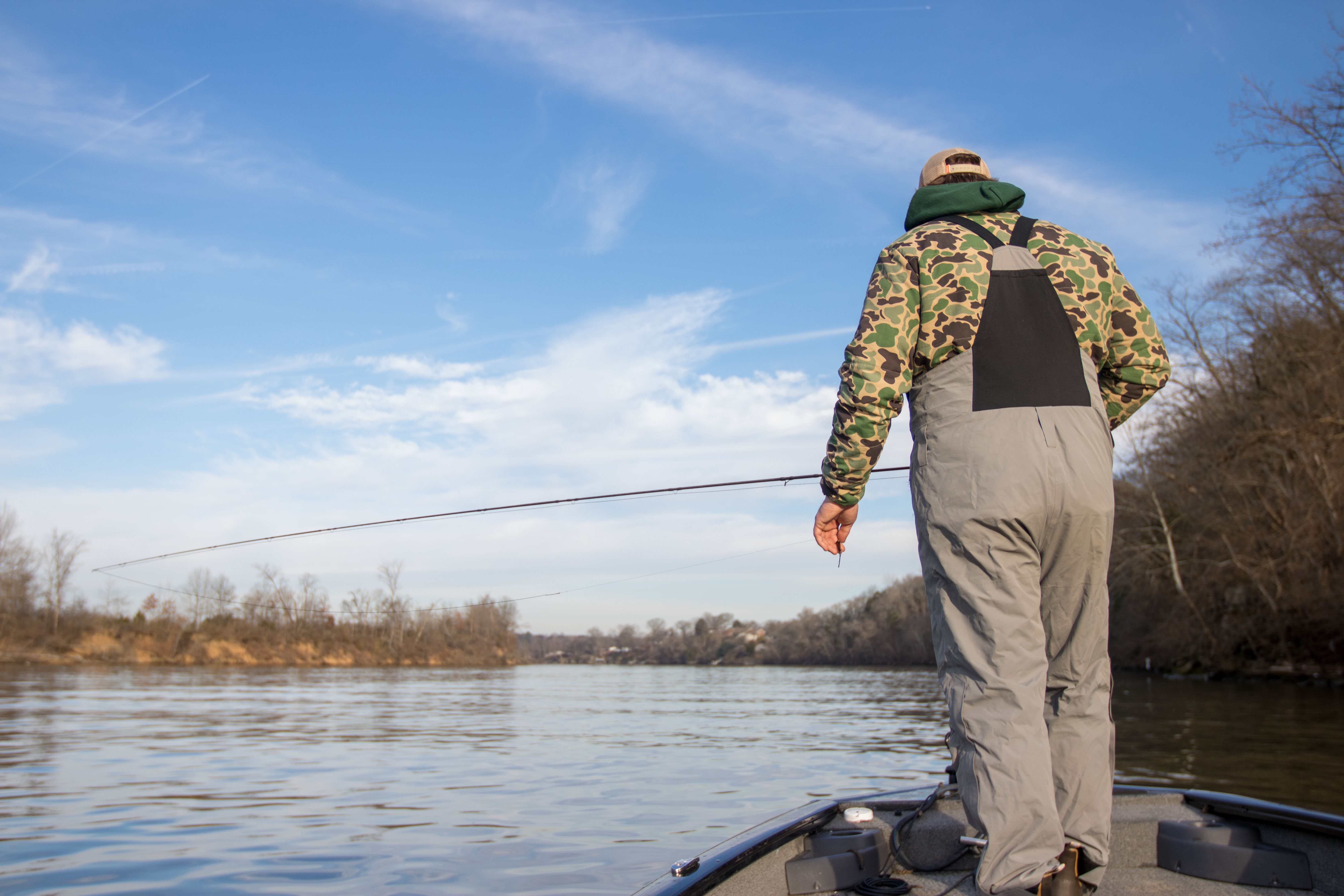 An angler holding a fly rod on a bass boat looking down at the water.