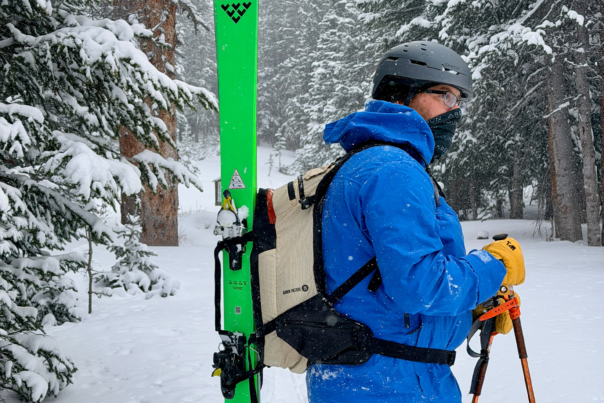 A skier wearing the Dawn Patrol 25 pack with skis attached vertically on the back