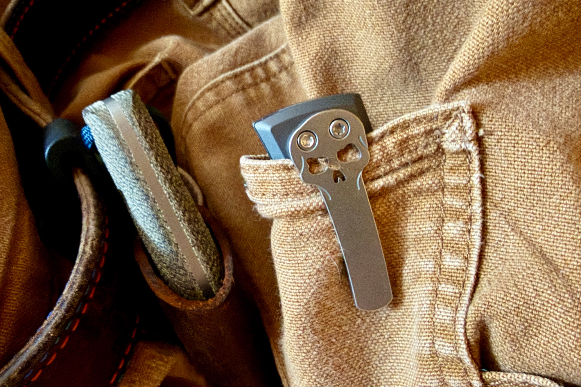 The skull clip visible as the knife is clipped to a pants pocket next to a leather sheath