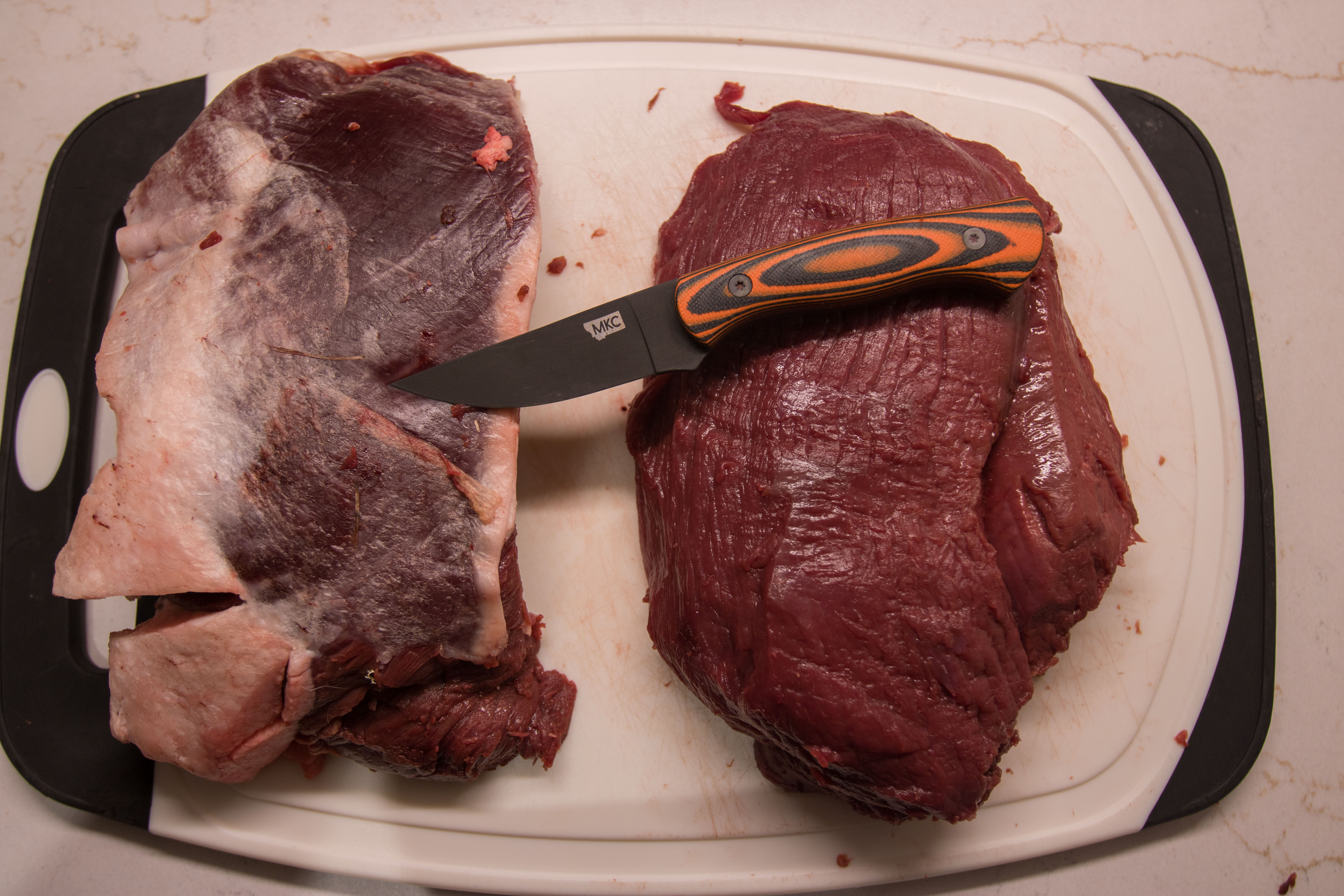 A knife laying on two cuts of meat on a cutting board.