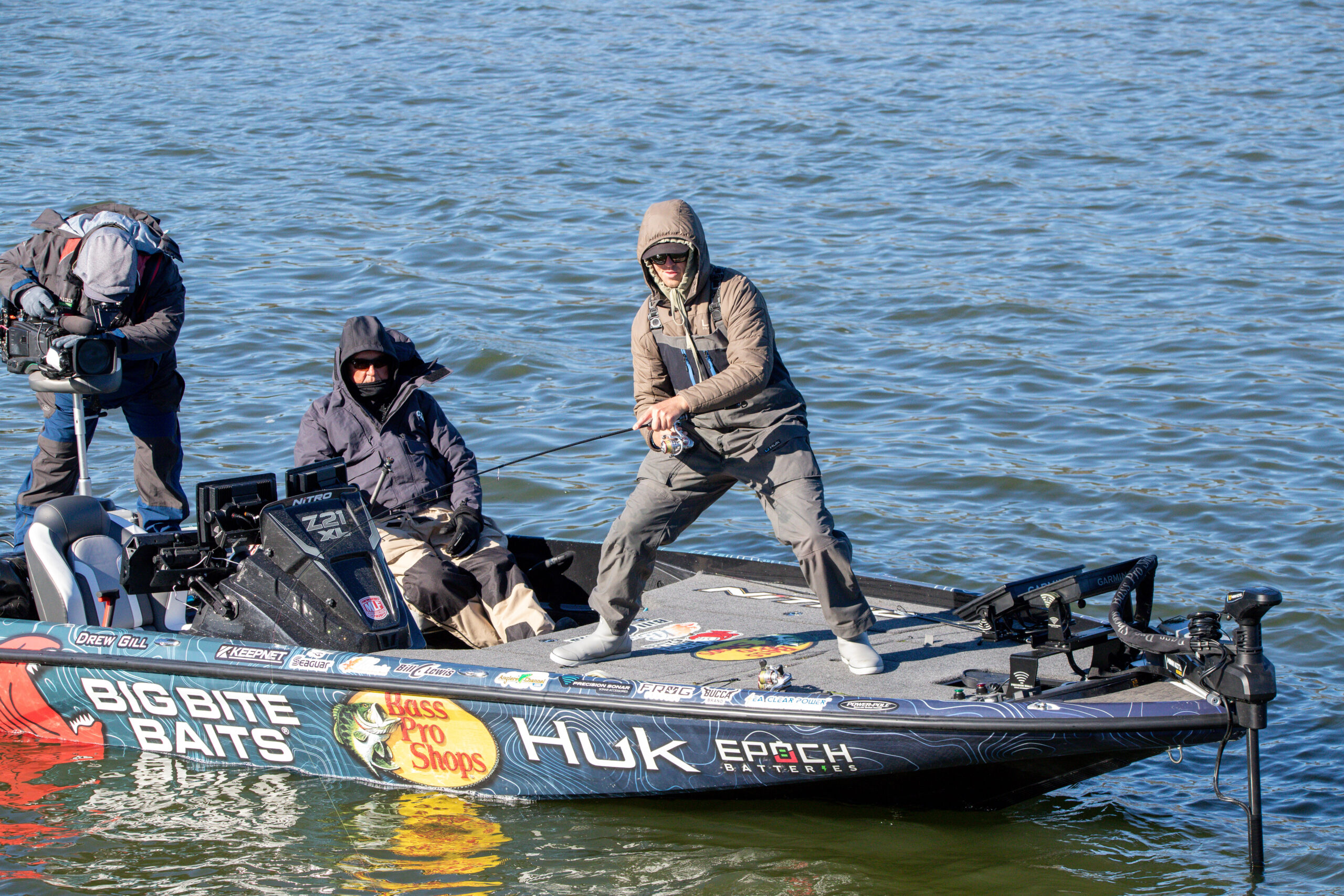 Drew Gill standing on the side of his boat, relling in a fish with a wide stance.