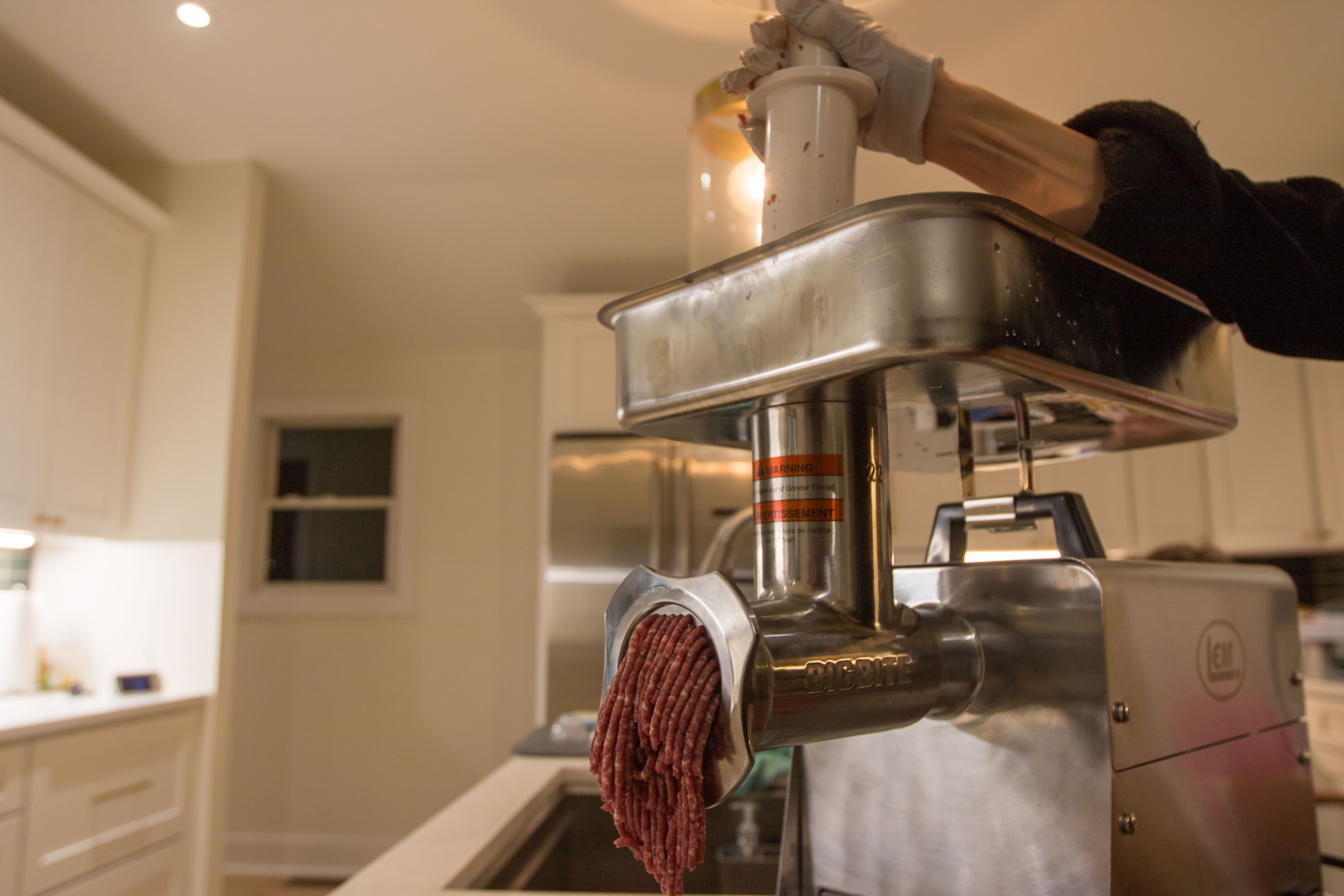 Ground meat coming from the LEM Big Bite #22 1.0 HP Meat Grinder in a kitchen.