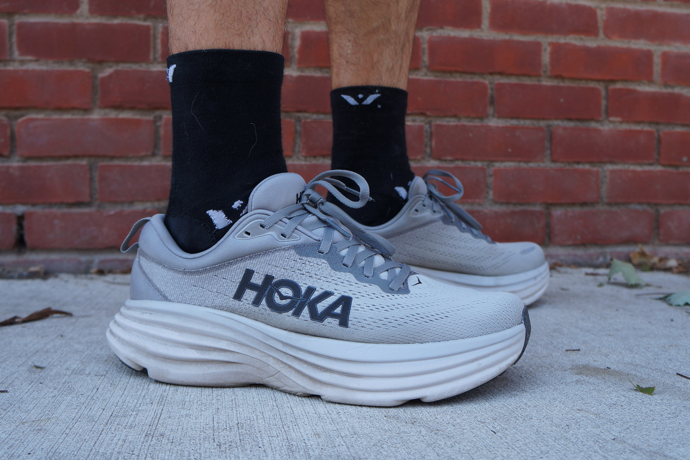 a runner wearing the gray Hoka Bondi 8 with black crew socks with a brick wall in the background