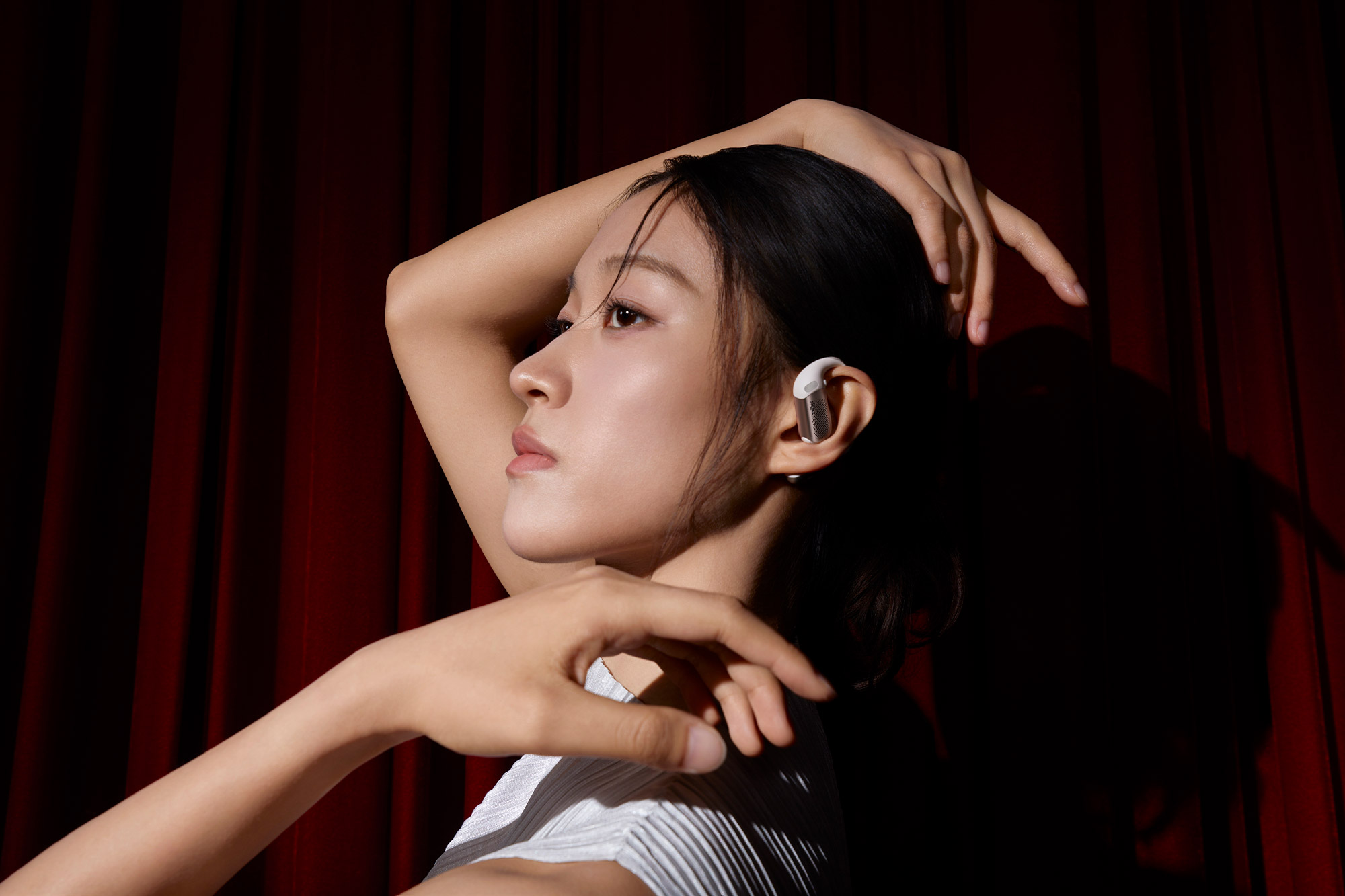 A woman wears the Shokz OpenFit Pro earbud while posing against a dark background
