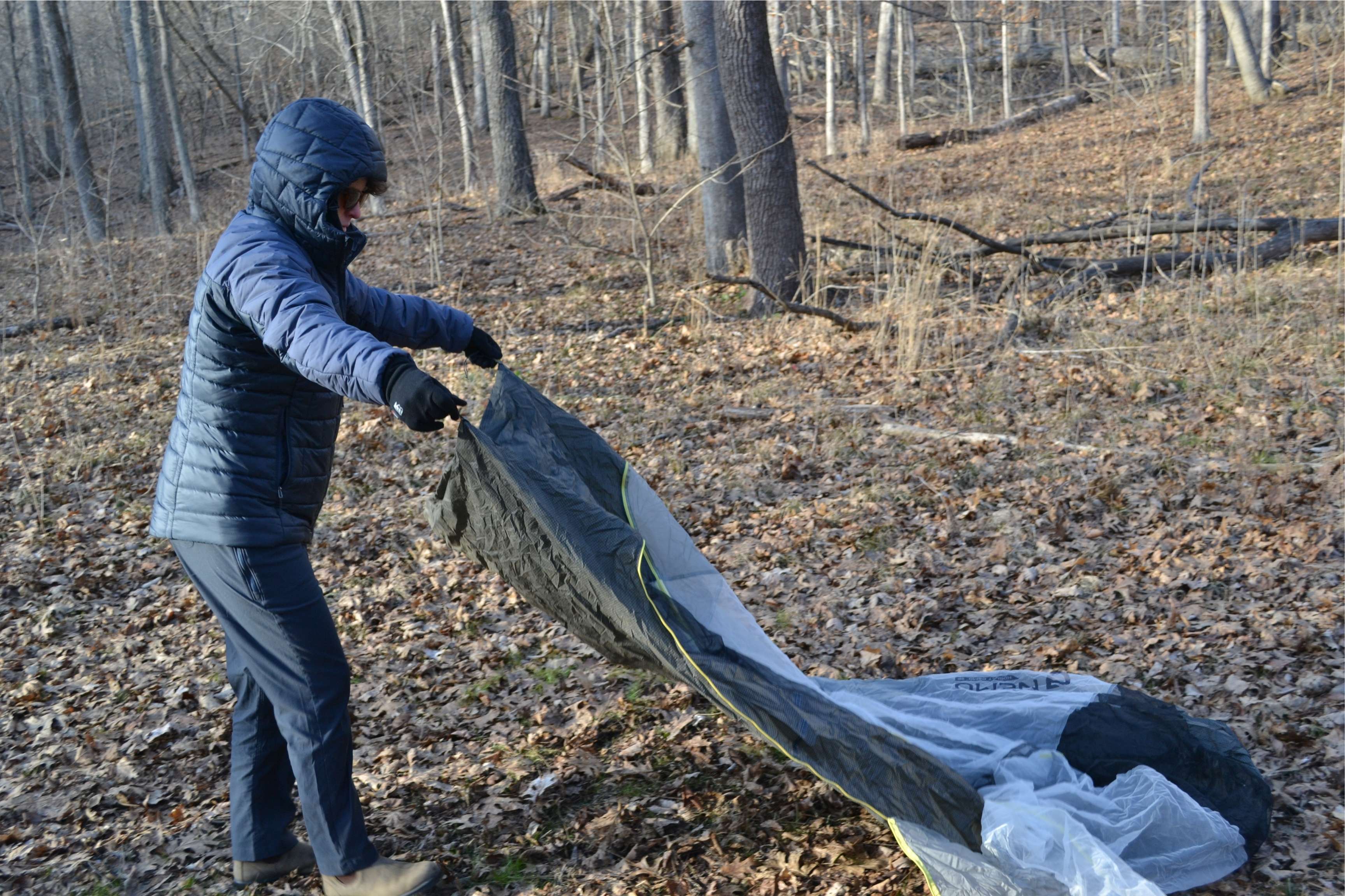 person setting up tent in woods