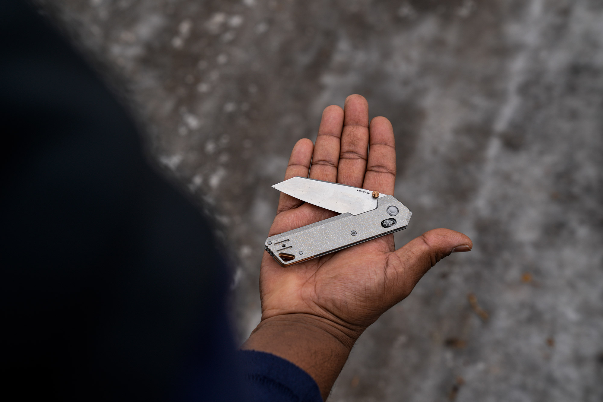 The folding knife shown open while resting in an adult hand for size reference