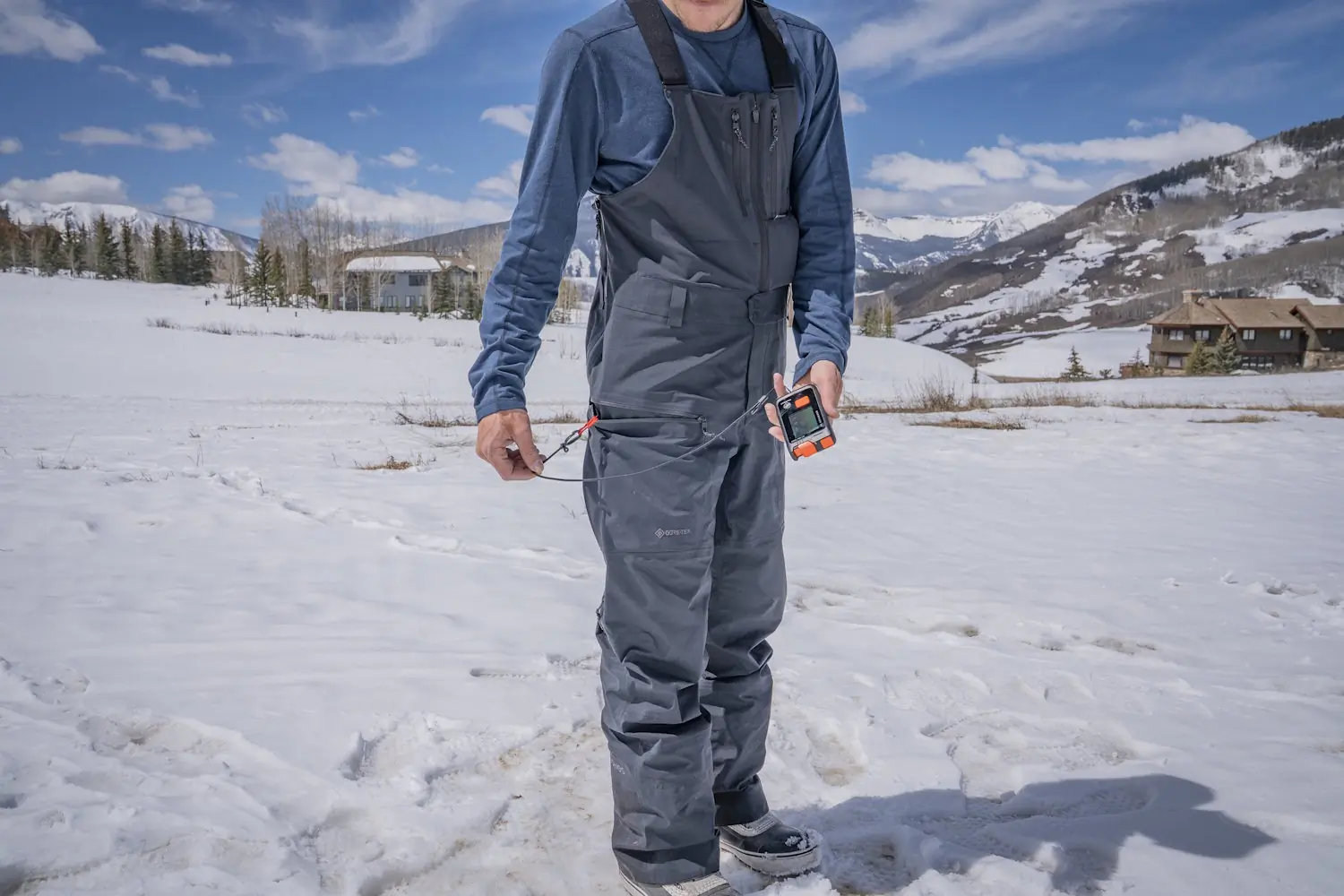 Man wearing Jones Shralpinist Recycled GORE-TEX ePE Bibs holding a beacon from a thigh pocket.