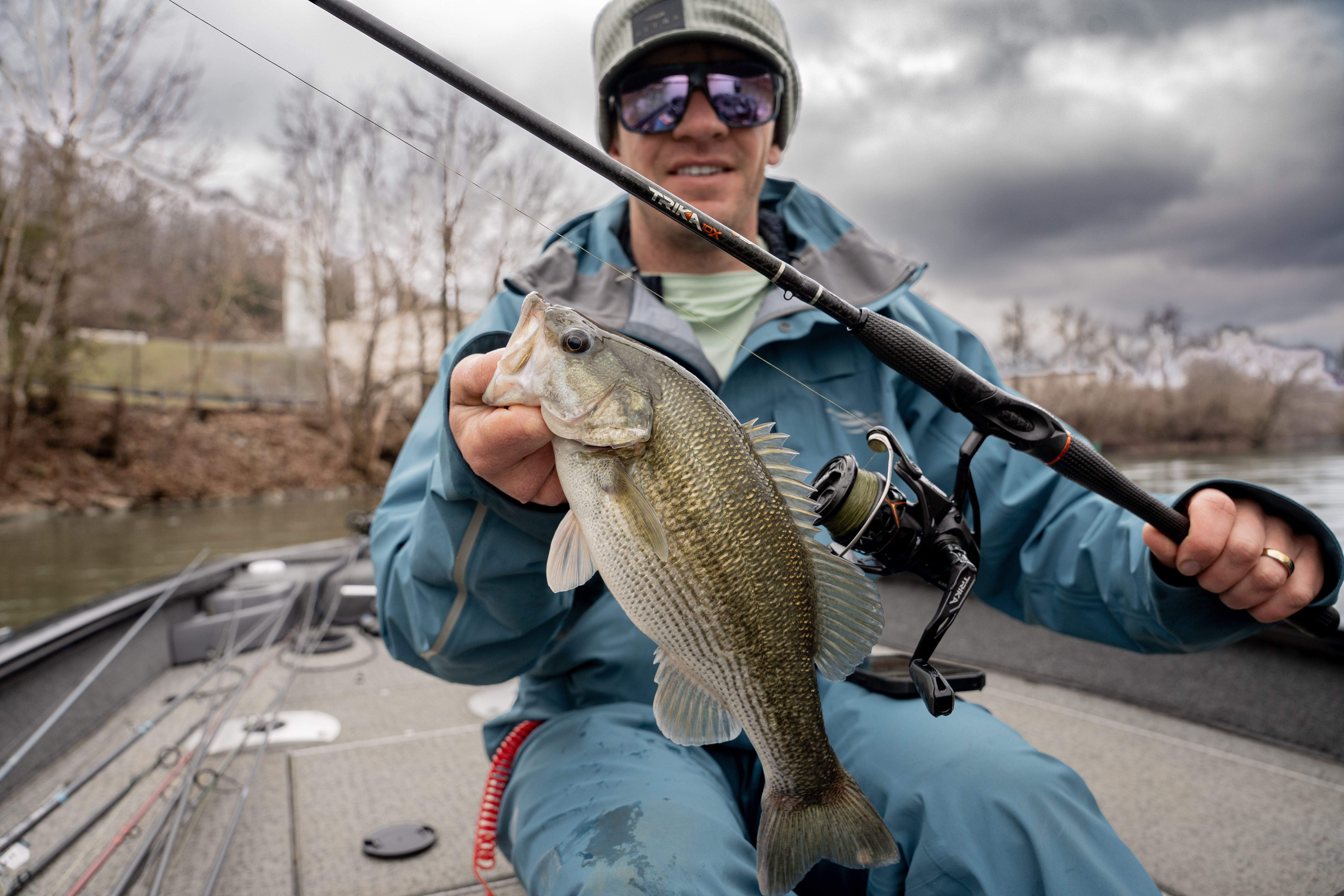 An angler holding a bass next to a fishing rod.